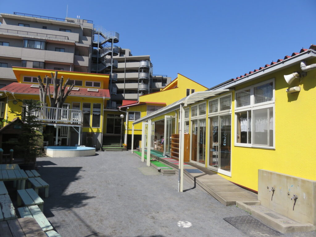 施設の中庭・外構。黄色い建屋と奥の住棟、晴天の屋外スペース