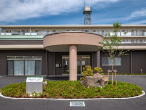 介護施設の玄関・車寄せ。モダンな半円形の屋根構造と整備された庭園が特徴。
